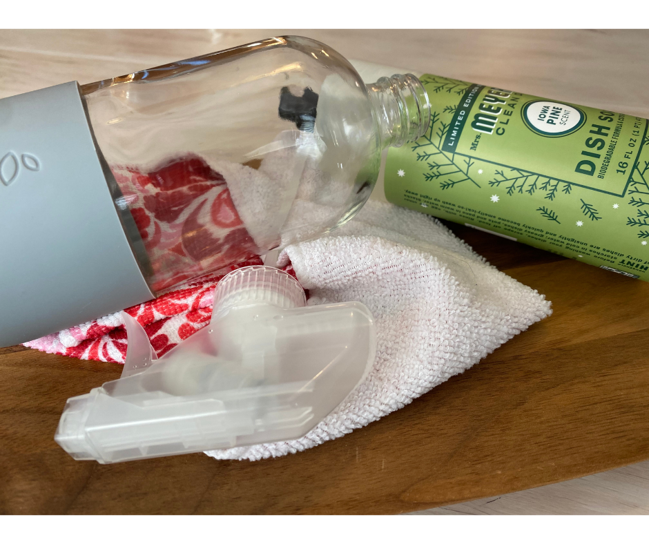 glass bottle, dish soap, rag, and spray nozzle laying on wood cutting board